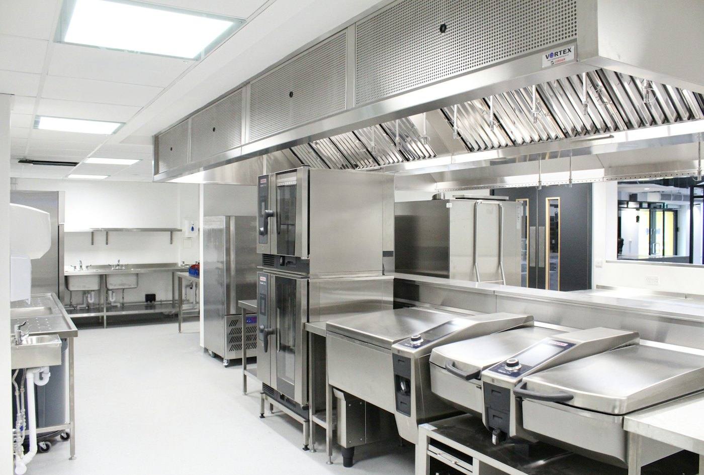 Bright stainless-steel commercial kitchen with ventilation hood